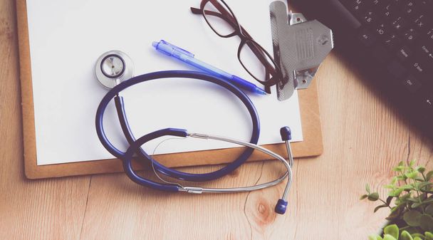lékařský fonendoskop u notebooku na dřevěný stůl, na bílém - Fotografie, Obrázek