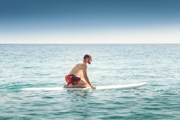 Um homem aprende a montar uma prancha de água em mar aberto
 - Foto, Imagem