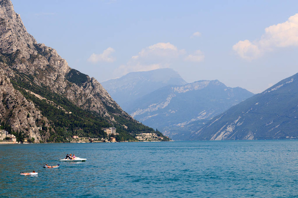 Lago de Garda y panorama de montaña con barco y personas relajantes en el aire acondicionado en Limone, Italia
 - Foto, Imagen