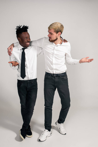 Χαρούμενη χαλαρή Αφρικής και Καυκάσιων αγόρια σε άσπρο και μαύρο γραφείο ρούχα γελώντας και θέτοντας σε λευκό φόντο στούντιο με αντίγραφο χώρου - Φωτογραφία, εικόνα