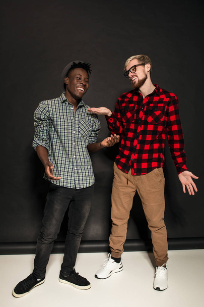 Studio lifestyle portrait of two best friends hipster boys going crazy and having great time together. On black background. - Photo, image