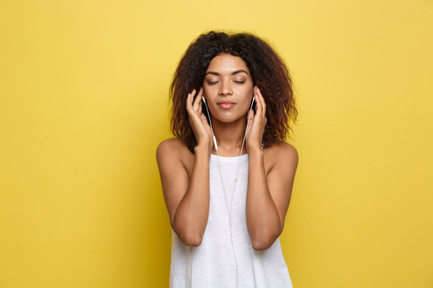 Lifestyle Concept - Portrait d'une belle femme afro-américaine qui écoute de la musique sur son téléphone portable. Fond jaune pastel studio. Espace de copie - Photo, image