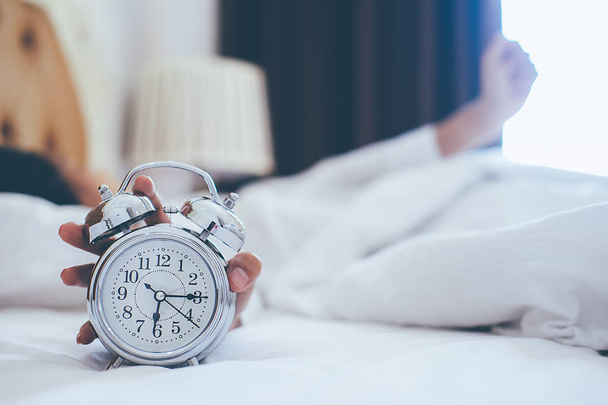 Раздраженная молодая женщина, откладывающая будильник на утро
 - Фото, изображение