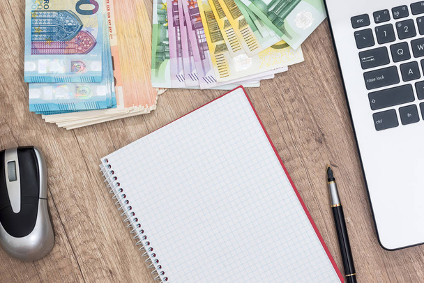 laptop, pen, euro banknote and notepad on desk. - Photo, Image