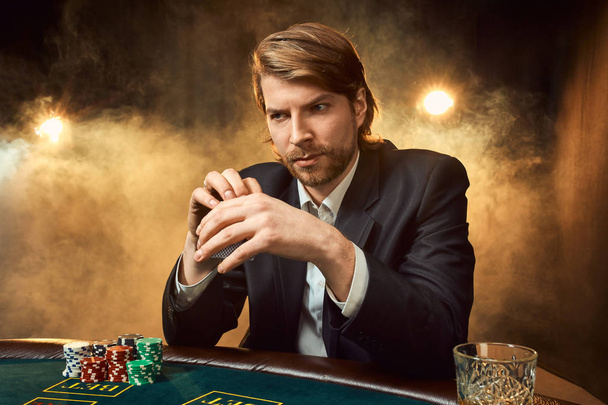 Ένας άντρας σε ένα επαγγελματικό κοστούμι που κάθεται στο τραπέζι του παιχνιδιού. Αρσενικό φορέας. Πάθος, κάρτες, μάρκες, αλκοόλ, ζάρια, τα τυχερά παιχνίδια, καζίνο - είναι ως αρσενικό ψυχαγωγία. - Φωτογραφία, εικόνα