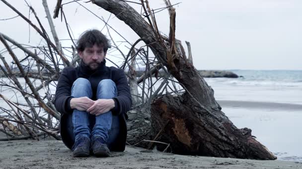 Θλιβερός θυμωμένος άνθρωπος κάθεται μπροστά στον ωκεανό το χειμώνα - Πλάνα, βίντεο