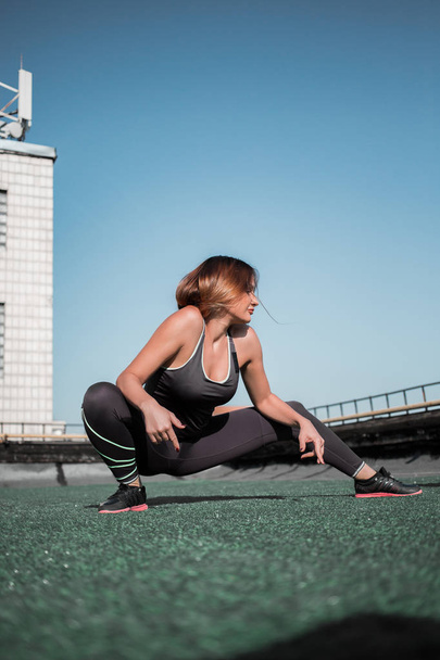 Young sportive woman doing deep lunges on the roof. - Photo, image
