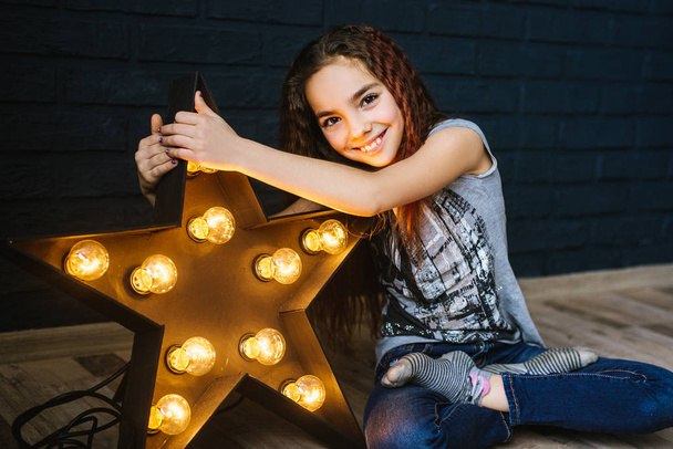 Une petite fille aux longs cheveux foncés avec une étoile qui brille dans ses mains. Le concept de renommée, chance, célébrité
 - Photo, image