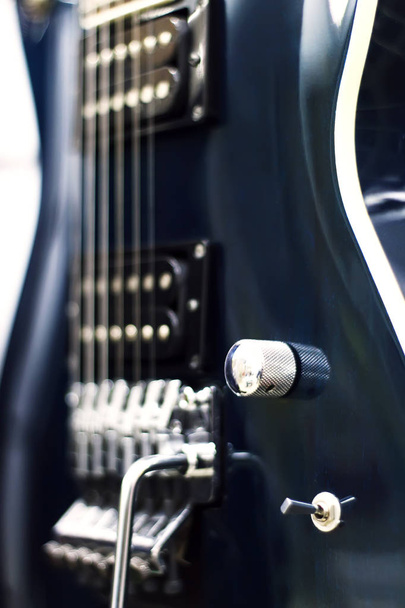Detalhe de uma guitarra elétrica preta chave baixa com luz suave e profundidade de campo
  - Foto, Imagem