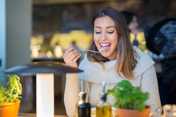 Hermosa mujer comiendo en un restaurante mientras sonríe
 - Foto, Imagen