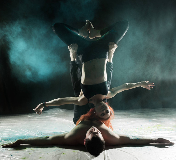 sports man and woman doing acroyoga exercises in a dark room with colorful smoke - Foto, imagen