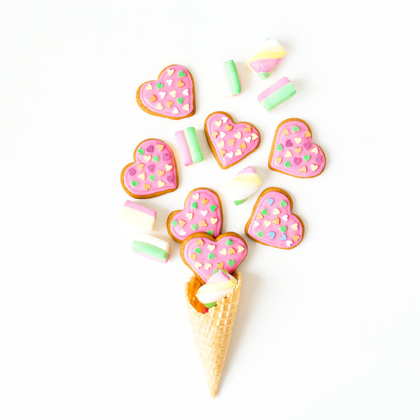 Biscuits avec glaçure rose et guimauves en cône de gaufre sur fond blanc. Composition d'amour. Pose plate. vue de dessus
. - Photo, image