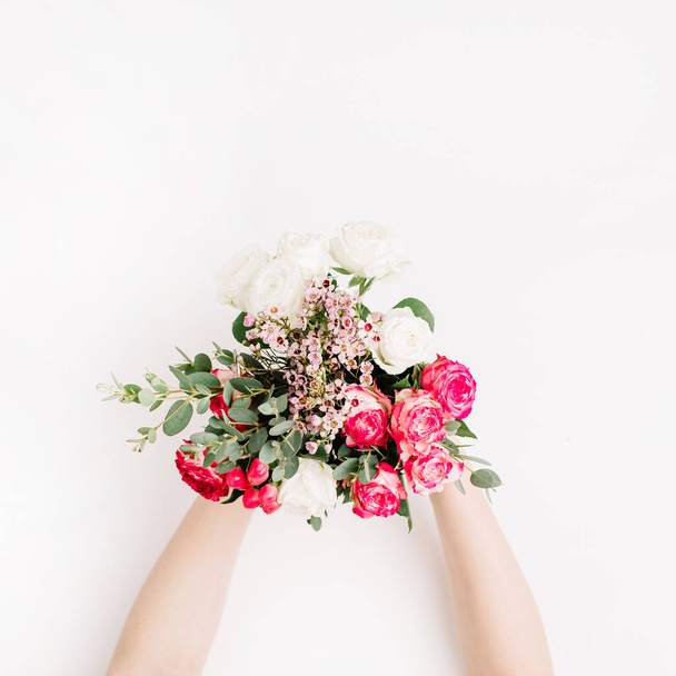 Mãos de mulher segurando buquê de casamento com rosas brancas, rosa e vermelhas, ramo de eucalipto, flores silvestres no fundo branco. Flat lay, vista superior conceito de casamento festivo
. - Foto, Imagem