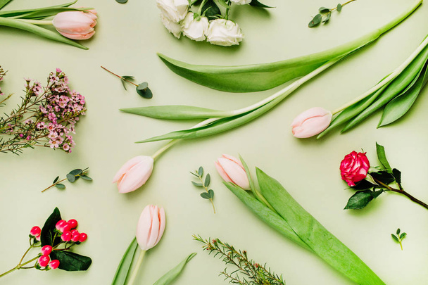 Flowers pattern made of pink tulips, roses, hypericum flower on green background. Flat lay, top view spring floral concept. - Photo, Image