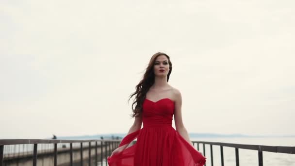 素晴らしい長い赤いドレスを着た女性が岸壁を歩いて幸せ - 映像、動画