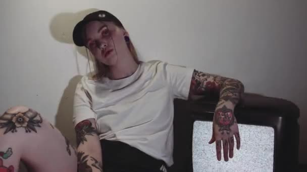 Женщина с панк-татуировкой сидела рядом с работающим статическим телевизором в темной комнате
 - Кадры, видео