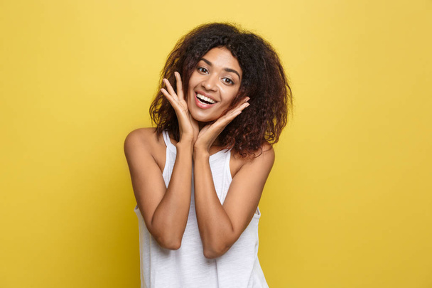 Sorrindo bela jovem afro-americana em t-shirt branca posando com as mãos no queixo. Estúdio filmado em fundo amarelo. Espaço de cópia
. - Foto, Imagem