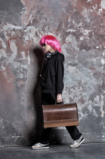 Woman in pink hair wig, headphones carry retro suitcase - Foto, afbeelding