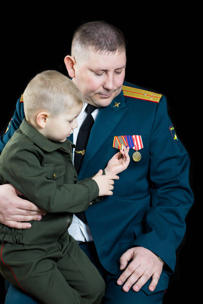 A small boy in military uniform looks at military medals. - Foto, imagen