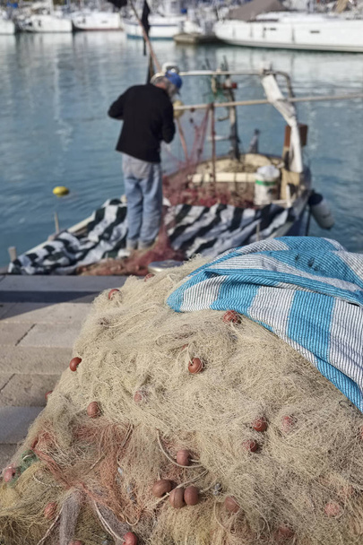 Italie, Sicile, Marina di Ragusa, filets de pêche et un pêcheur travaillant sur son bateau dans le port
 - Photo, image
