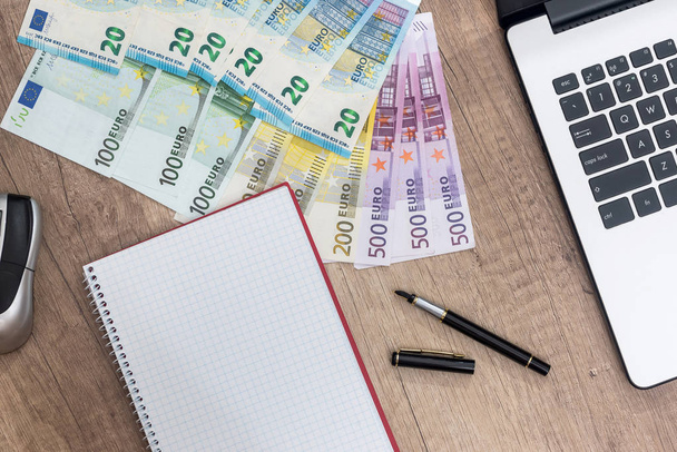 laptop, pen, euro banknote and notepad on desk. - Foto, afbeelding