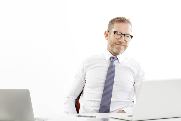 Studio portrait of investment businessman working on laptop while sitting at desk at isolated white background  - Foto, Imagen