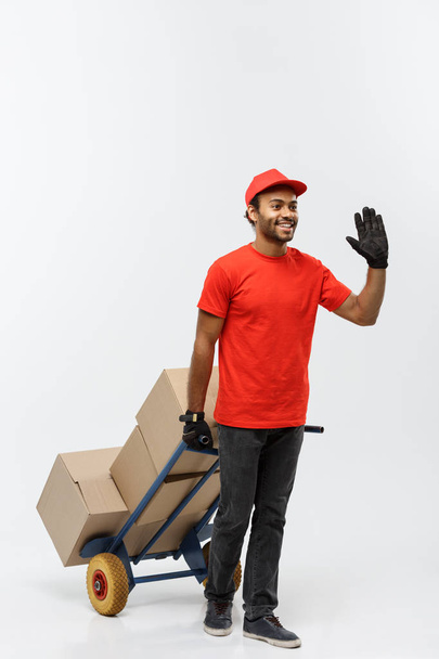 Delivery Concept - Portrait of Handsome African American delivery man or courier pushing hand truck with stack of boxes. Isolated on Grey studio Background. Copy Space. - Photo, Image
