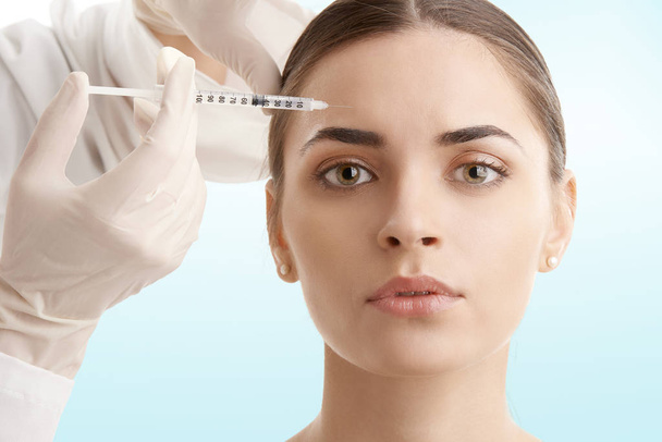 Portrait of an attractive young woman receiving botox treatment. Isolated on light blue background.  - Photo, image