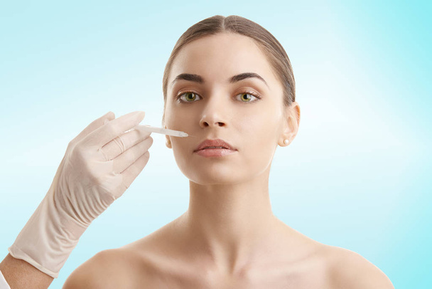 Portrait of an attractive young woman receiving lip augmentation treatment. Isolated on light blue background. - Foto, afbeelding