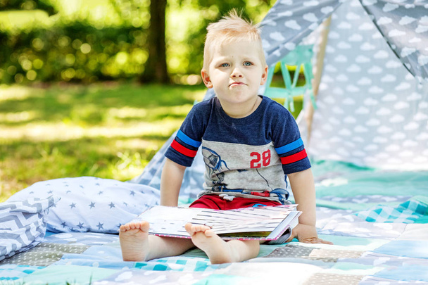 Το παιδί είναι δυσαρεστημένος με ένα βιβλίο στο πάρκο. Preschooler αγόρι  - Φωτογραφία, εικόνα