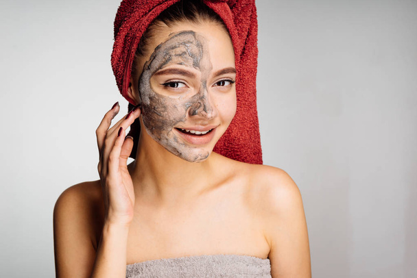 happy young girl with a towel on her head applied a useful clay mask to half the face - Valokuva, kuva