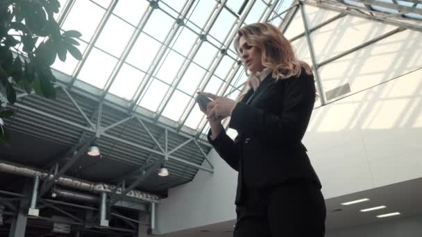 young woman in a business suit uses a mobile phone. business woman is texting a message on the smartphone in the office building. - Video, Çekim