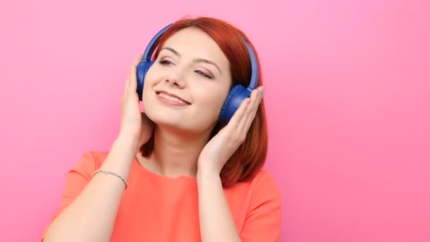 Χαμογελώντας κοκκινομάλλα ακρόαση μουσικής στο ακουστικό της νεαρής γυναίκας - Πλάνα, βίντεο