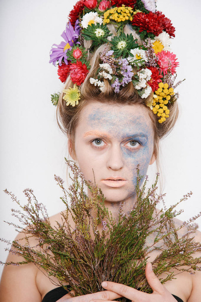 A young woman with flowers on her head and hands. Spring image with flowers. Man with a colorful plant. The girl and the blooming haircuts and brocade on her face. - Foto, Bild