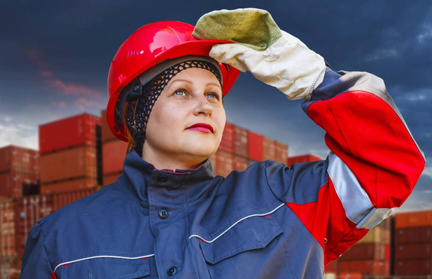  The woman in protective working clothes. labor protection .Under construction . Work safety .A helmet for protection of the head . A helmet for protection of the head .  Working gloves . Industrial protective wear . Stacked cargo containers in port  - Photo, Image