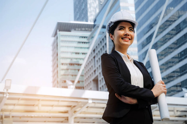 young asian business, engineer or technician woman in suit with white safety helmet looking to future and arms crossed in big city building background, business, industry and construction concept - Фото, зображення