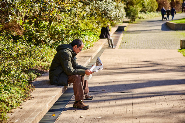 Lisszabon, Portugália - január, 2018. Gulbenkian parkban és a kertben. A parkban egy ember ül, és újságot olvas. A kertben ember ül a járdára, és tanulmányok egy poszter. - Fotó, kép