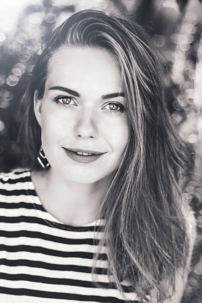 Black and white portrait of beautiful smiling white Caucasian girl woman with long hair wearing striped t- shirt outside in summer park looking in camera. - Foto, afbeelding