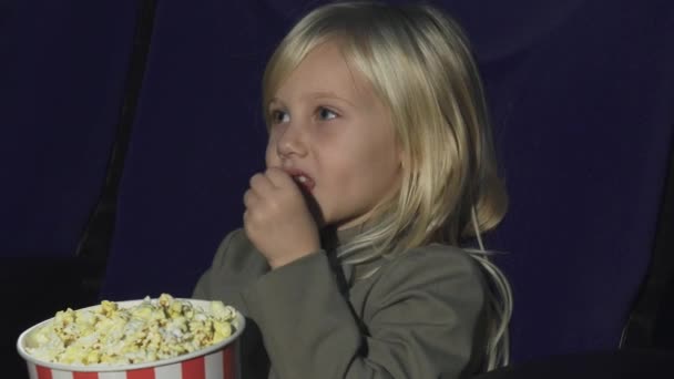 Zbliżenie na urocza dziewczynka jedzenie popcorn w kinie - Materiał filmowy, wideo