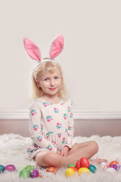 Söpö ihana valkoihoinen lapsi tyttö yllään pääsiäispupu kani korvat istuu pehmeällä pörröinen matto matto studiossa. Lapsi tilalla loma värikkäitä munia juhlii perinteistä pyhää kristillistä lomaa
  - Valokuva, kuva