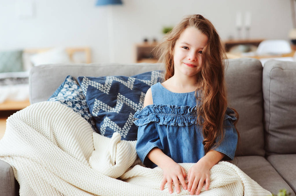 cute little child girl relaxing at home, sitting on couch, wrapped in cozy blanket. Kids health and seasonal flu healing concept - Фото, изображение