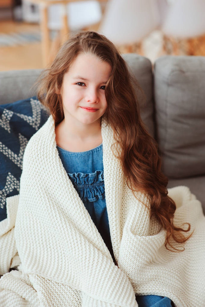 cute little child girl relaxing at home, sitting on couch, wrapped in cozy blanket. Kids health and seasonal flu healing concept - Valokuva, kuva