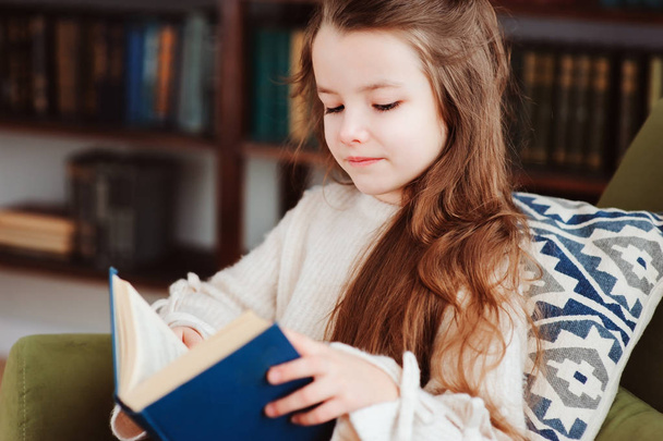 happy smart schoolgirl reading books in library or at home. Kids early learning and education concept. - Foto, Imagem