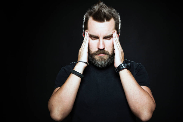 Terrible headache. Frustrated man touching head with hands and making face while standing against black background. Copy space for text - Photo, Image