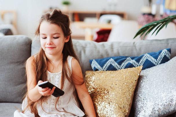 child girl watching tv at home on cozy couch. Modern scandinavian interior, kids and television concept - Fotografie, Obrázek