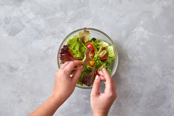 female hands eating healthy salad of vegetables on grey table - Foto, Imagen