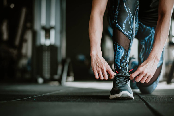 Обрізаний знімок жінки, що зав'язує шнурки перед тренуванням у спортзалі
 - Фото, зображення