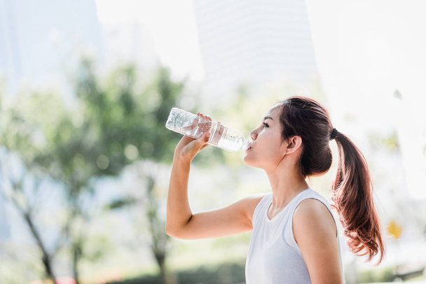 公園でジョギングした後の水のボトルから水を飲む若いアジア女性のショット. - 写真・画像