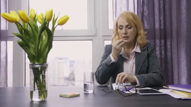 Senior woman taking pills from headache at office - Materiał filmowy, wideo