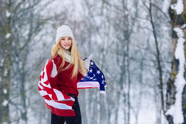 Retrato de invierno de una joven adolescente con bandera de Estados Unidos. Belleza Joyful Model Girl riendo y divirtiéndose en el parque de invierno. Hermosa joven al aire libre. Disfrutando de la naturaleza, el invierno
 - Foto, imagen